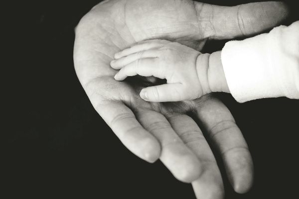 A parent's hand holding a baby's hand